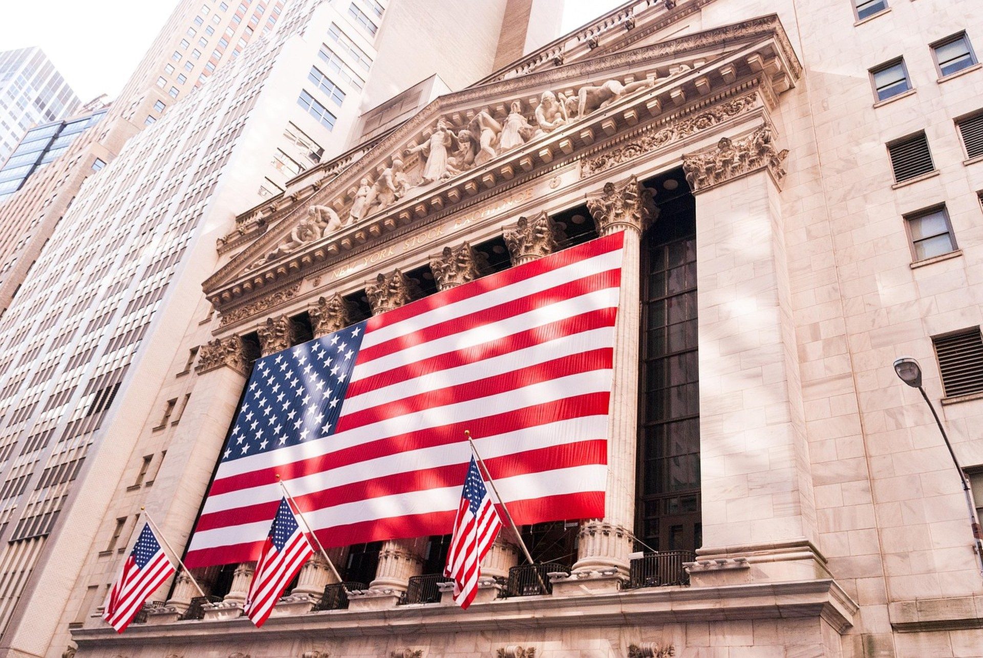 Класичний кам'яний фасад з колонами та фронтоном AMERICA STOCK EXCHANGE, великий американський прапор і три менші, обабіч су